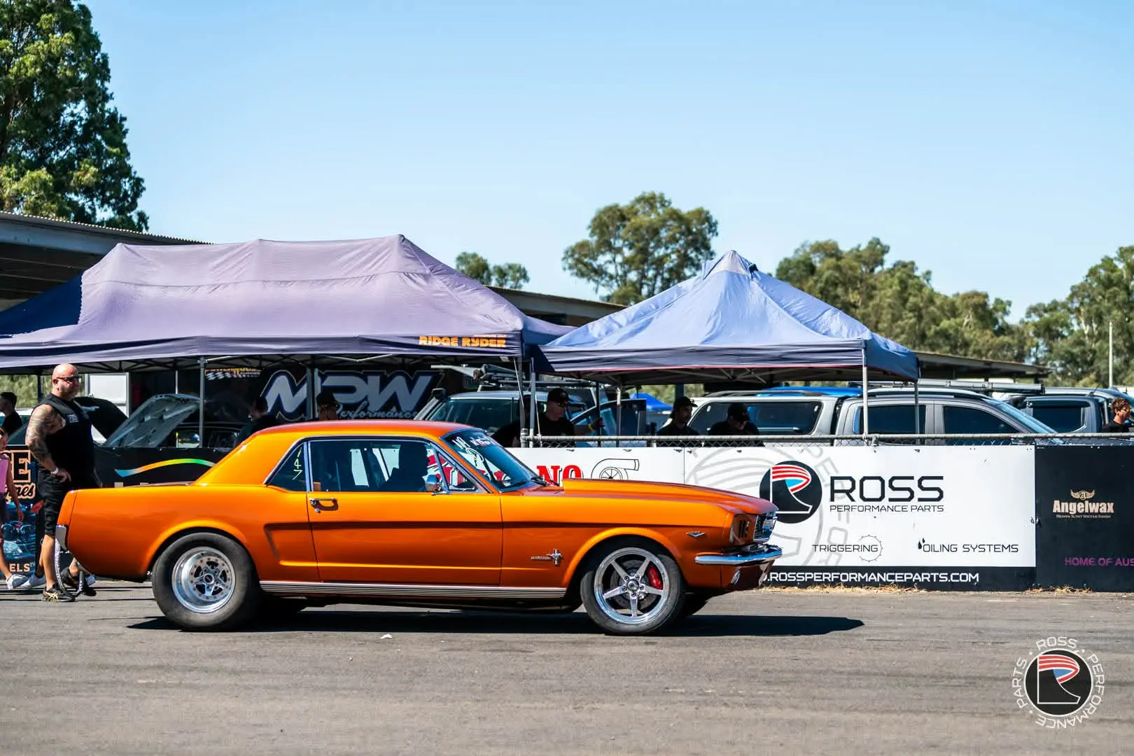 Orange classic Mustang at a motorsport event in front of Ross Performance Parts trackside signage