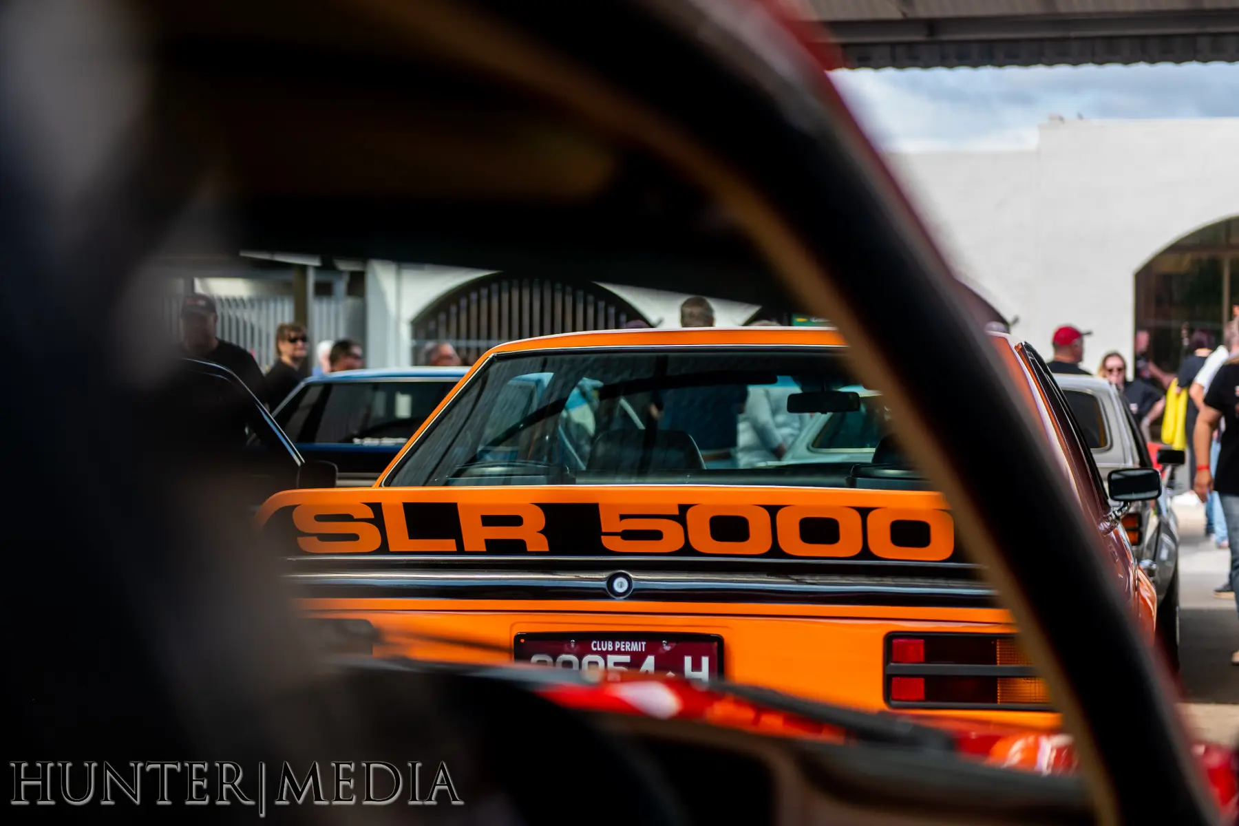 Orange SLR 5000 framed through another Torana at the event