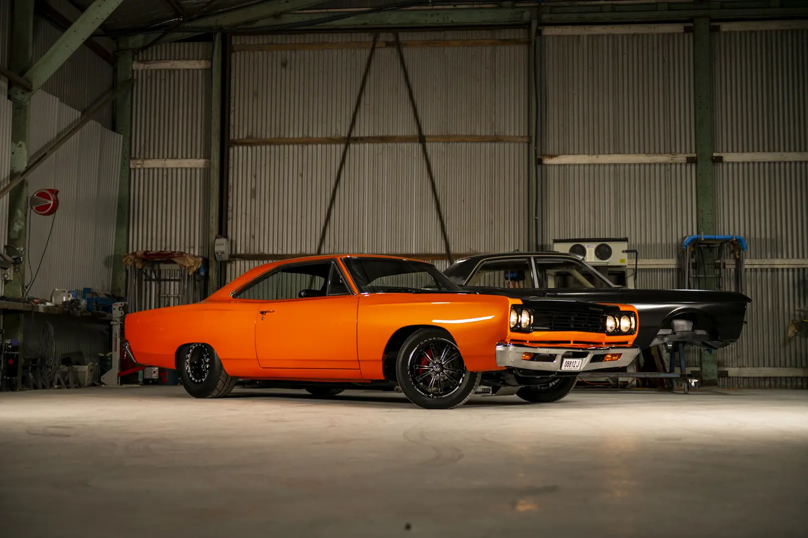 Orange and black classic muscle cars photographed inside a workshop