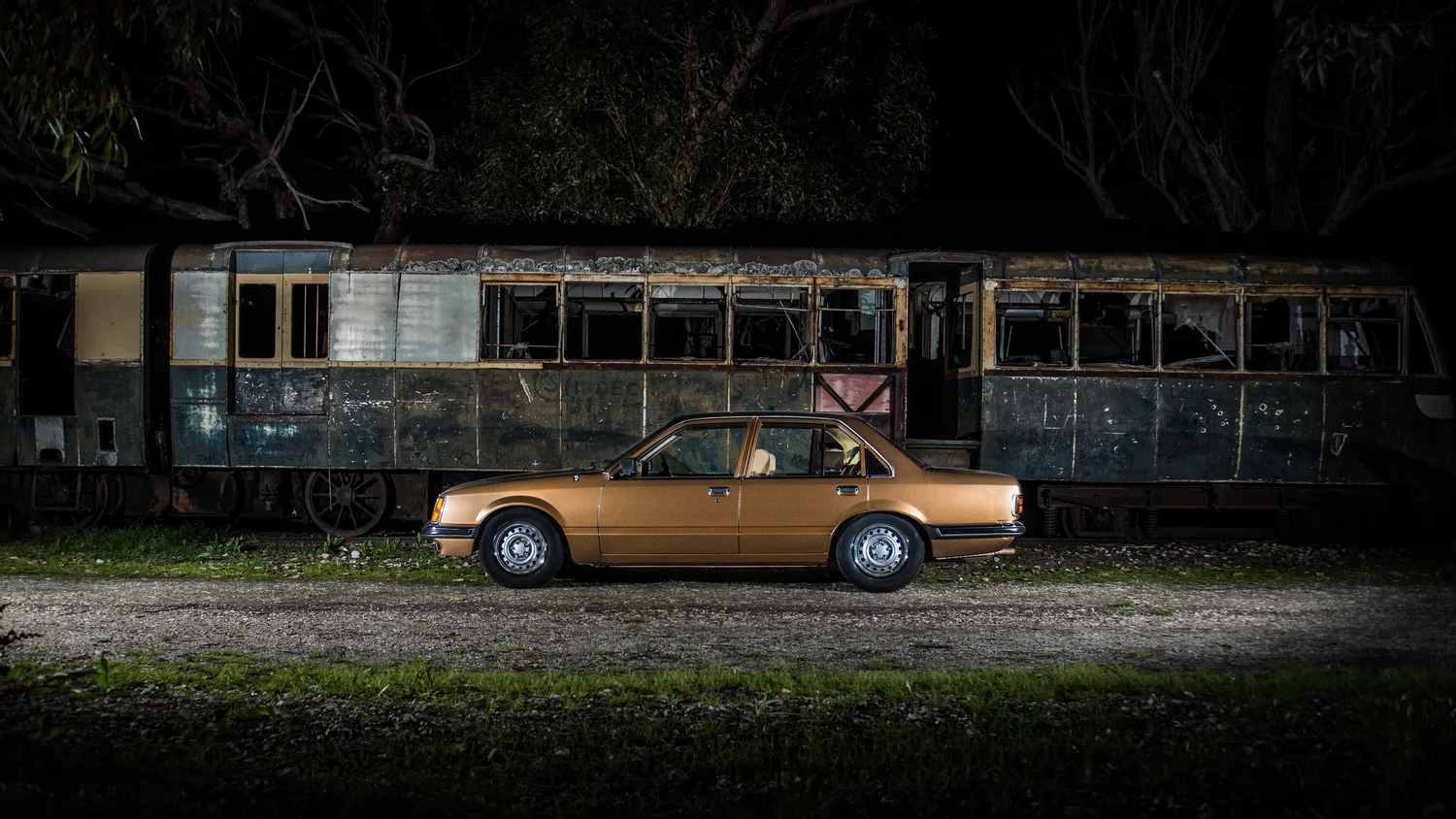 A classic car photographed beside a weathered rail carriage at night