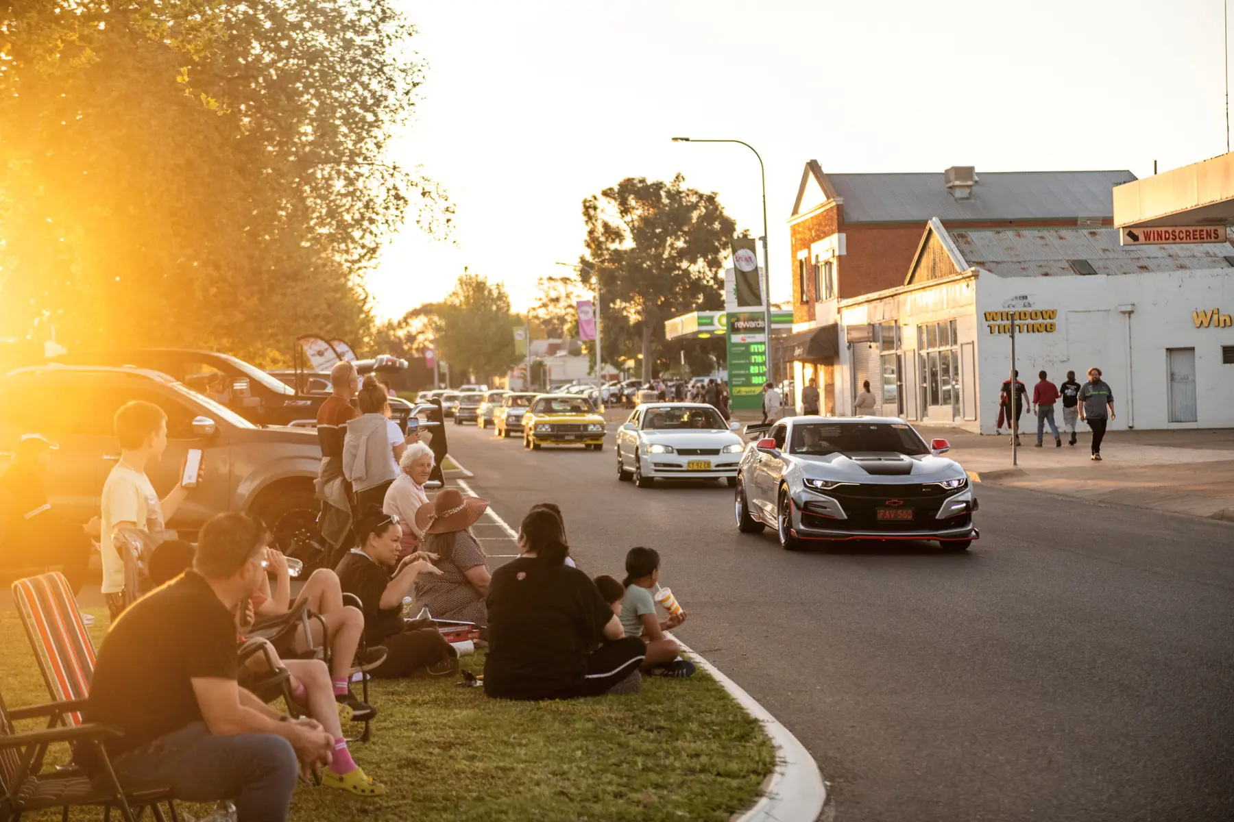 Performance cars cruising past spectators at sunset