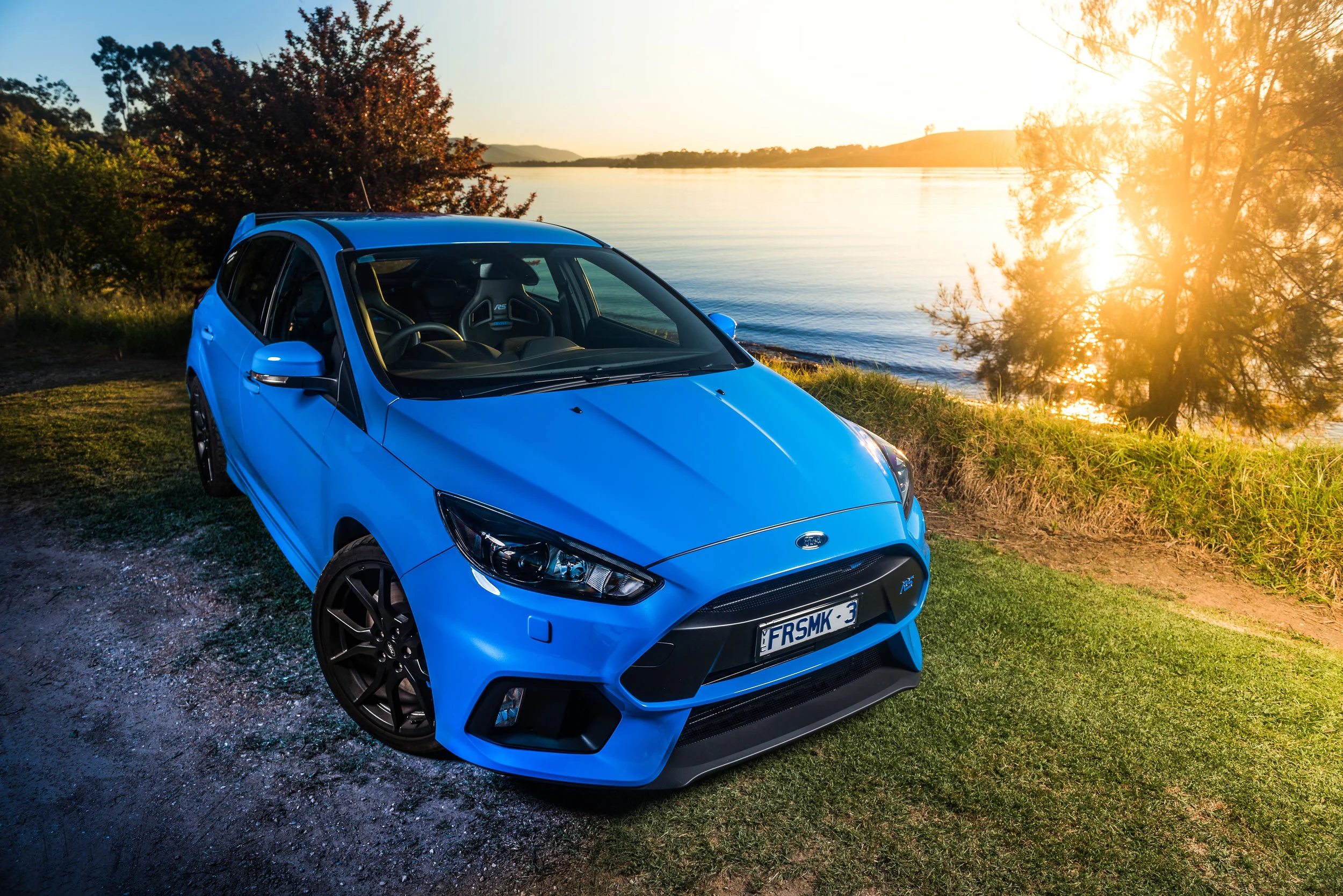 Blue performance car photographed beside a lake at sunset